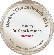 The image shows a circular badge with text and symbols on it. The badge features the year  2015  prominently at the top, followed by the words  Doctor s Choice Awards.  Below this title, there is a name  Dr. Goro Nazarian,  and underneath that, there is a profession listed as  Dentist.  At the bottom of the badge, it reads  Nominee  in capital letters. The text on the badge is clear and legible. In the center of the badge, there is an emblem with a shield and a crown above it. The background of the badge is white, and the border is a thin gold line. The overall style of the image is formal and professional, suggesting that the badge represents recognition or an award in the field of dentistry.