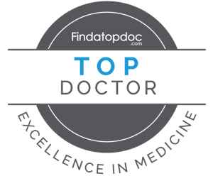 The image shows a logo with text that reads  TOP DOCTOR  above a circular emblem featuring a stethoscope, and below that, additional text states  FINDATOPDOC  followed by  EXCELLENCE IN MEDICINE.