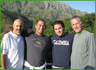 The image shows four men posing together outdoors with mountains in the background  they are smiling and appear to be enjoying their time together.