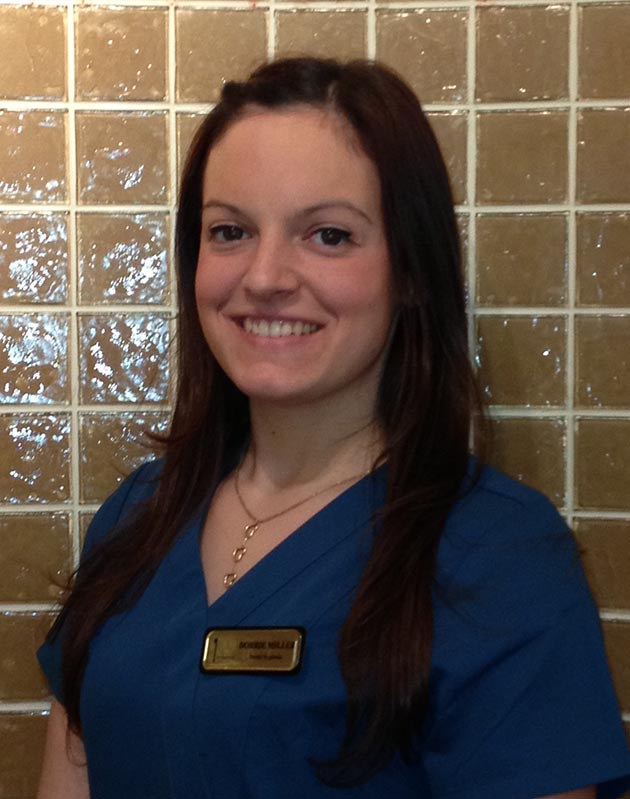 A woman wearing a blue uniform stands against a tiled wall.