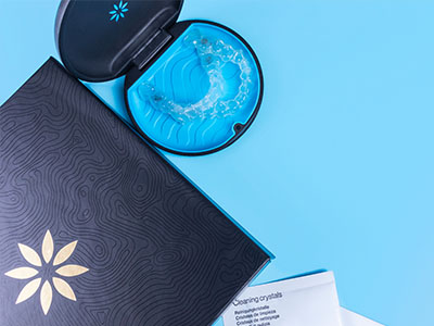 A close-up photograph of a blue toothbrush with bristles, placed on top of an open box of dental floss, set against a light blue background.