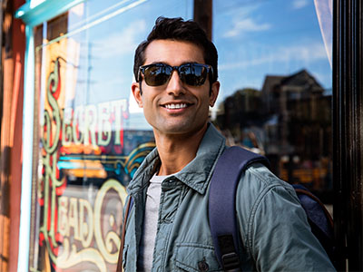 A young man with sunglasses stands confidently outside a storefront, posing for the camera.