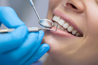 Woman receiving dental treatment with a smile, featuring a dentist s hand holding a dental tool, set against a blue background.