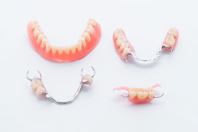 The image shows a set of dentures with pink teeth displayed on a white surface, accompanied by a single toothbrush with bristles.