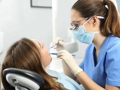 A dental hygienist is performing a cleaning procedure on a patient s teeth while wearing personal protective equipment.