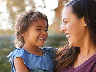 The image features a woman and a young child sharing a joyful moment together outdoors during daylight.