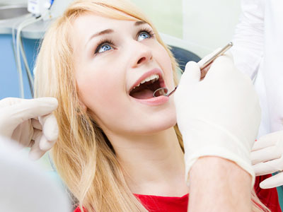 A woman sitting in a dental chair receiving dental care, with a dentist holding tools over her open mouth.