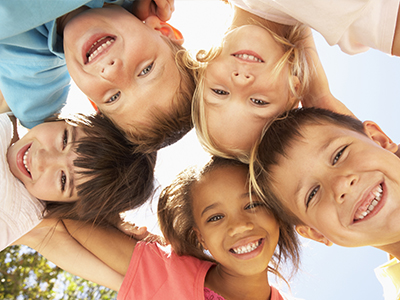 A group of children posing together with smiles, under a bright sky.