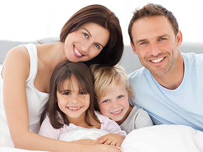 A family of four posing together on a bed with a white comforter.